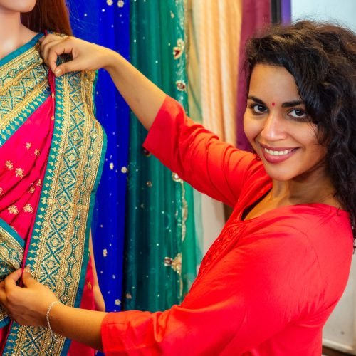 brunette indian woman choosing a new tradition saree in market.needlewoman designer drapery fabric dress on a mannequin.